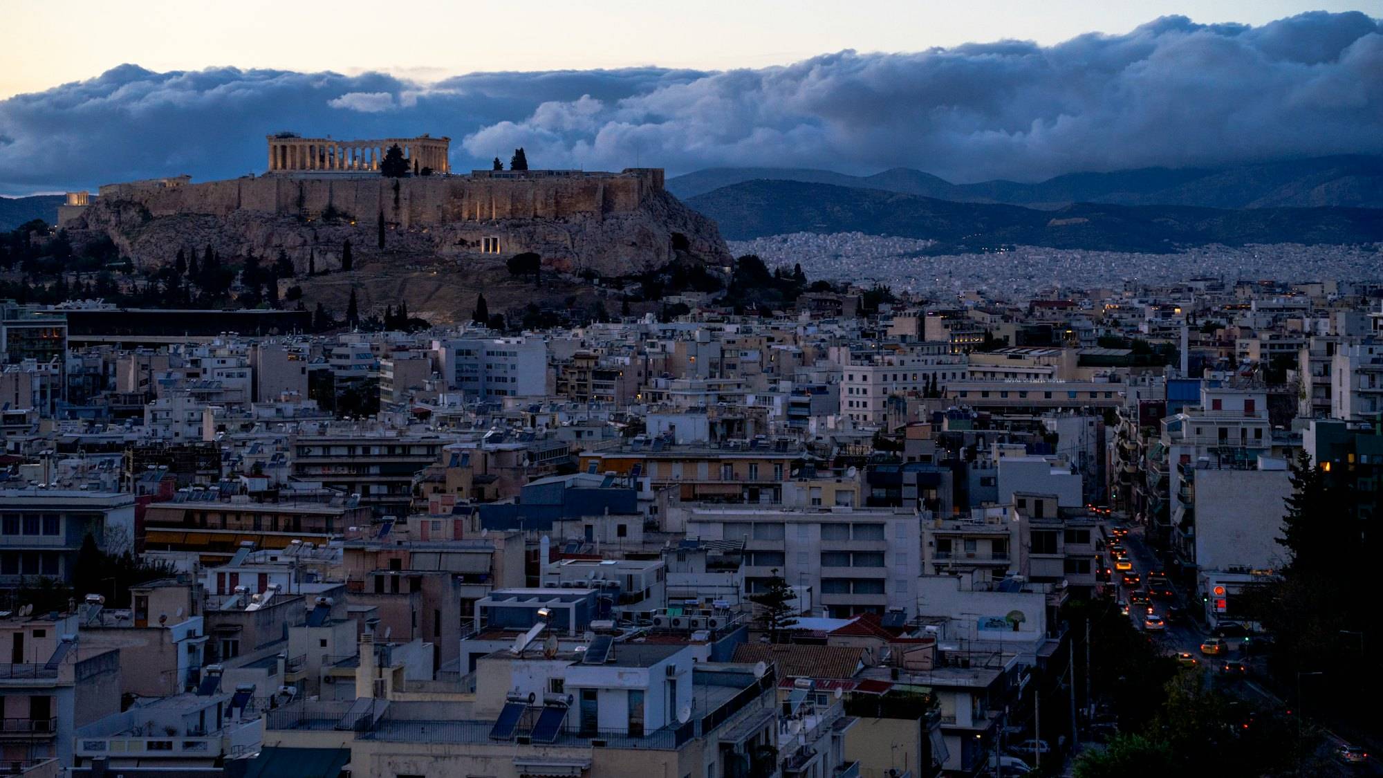 The Acropolis above central Athens at dusk, with apartment blocks spreading to the hills