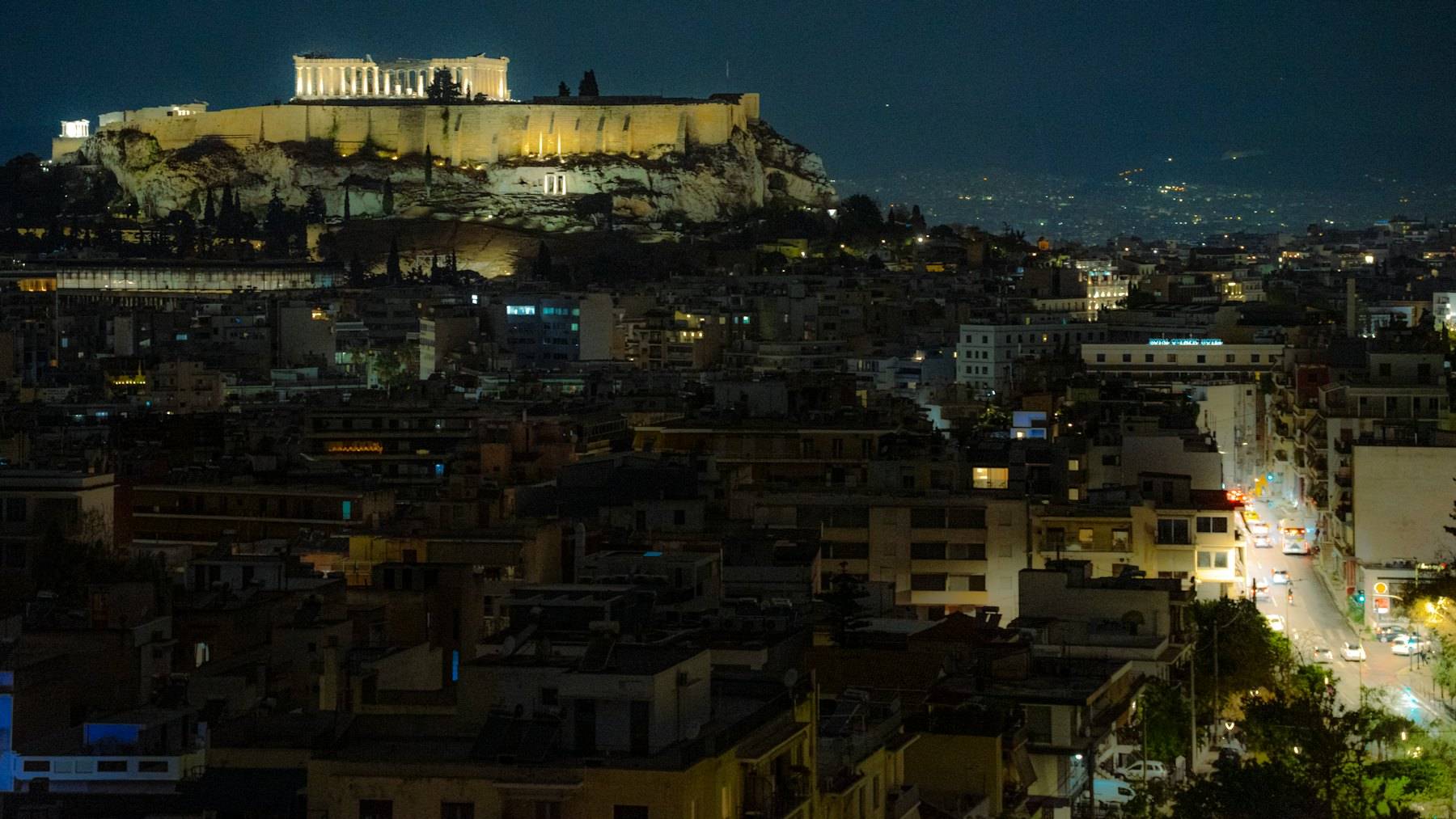 The Acropolis lit up at night above the streets of Athens